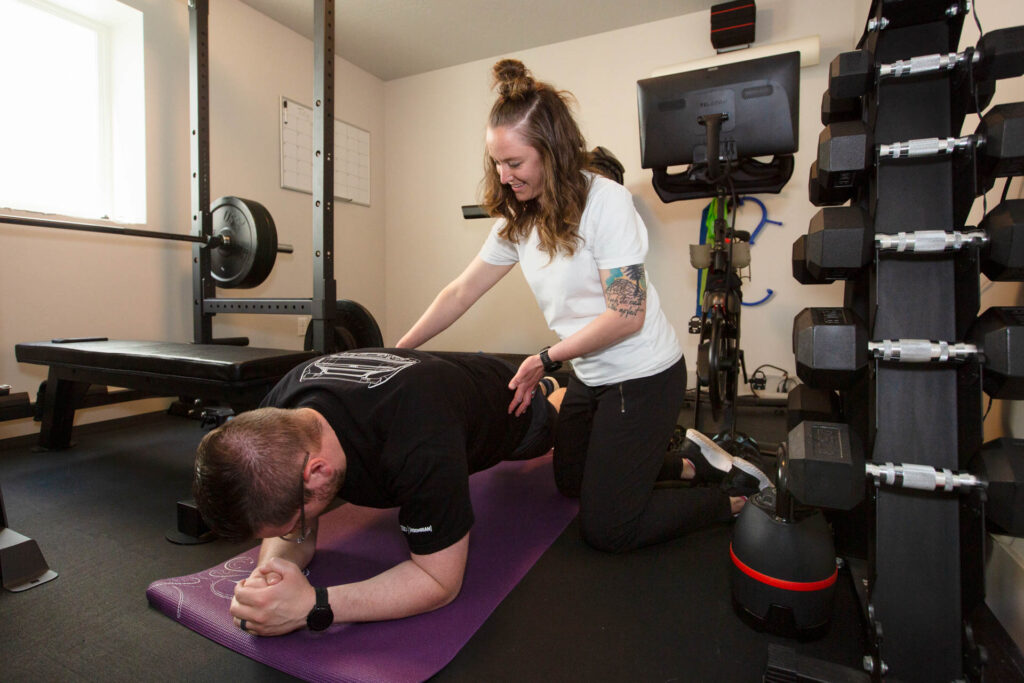 A person doing a forearm plank on a yoga mat being assisted by their coach.